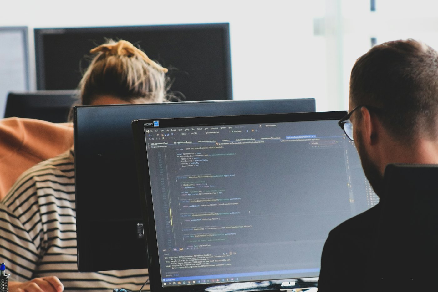 Developers working on code across two monitors in a bright office