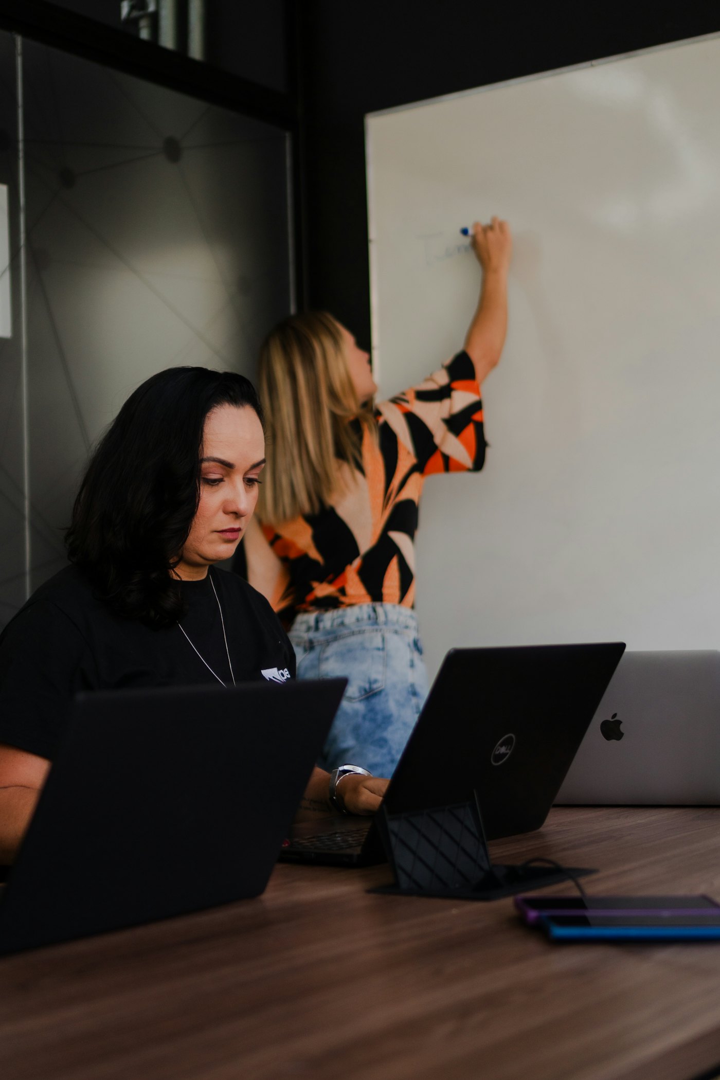Two colleagues working on laptops beside a whiteboard
